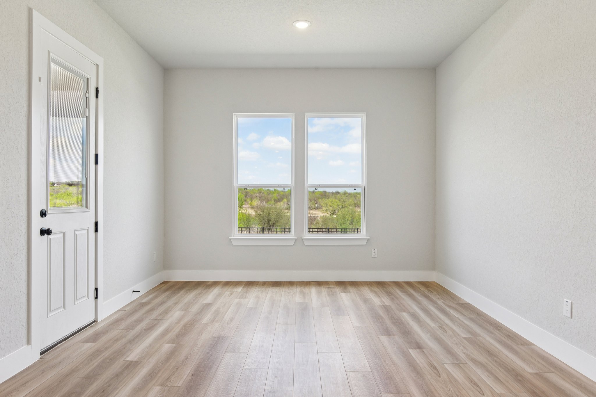 A room with a wood floor and a window with a view of trees.