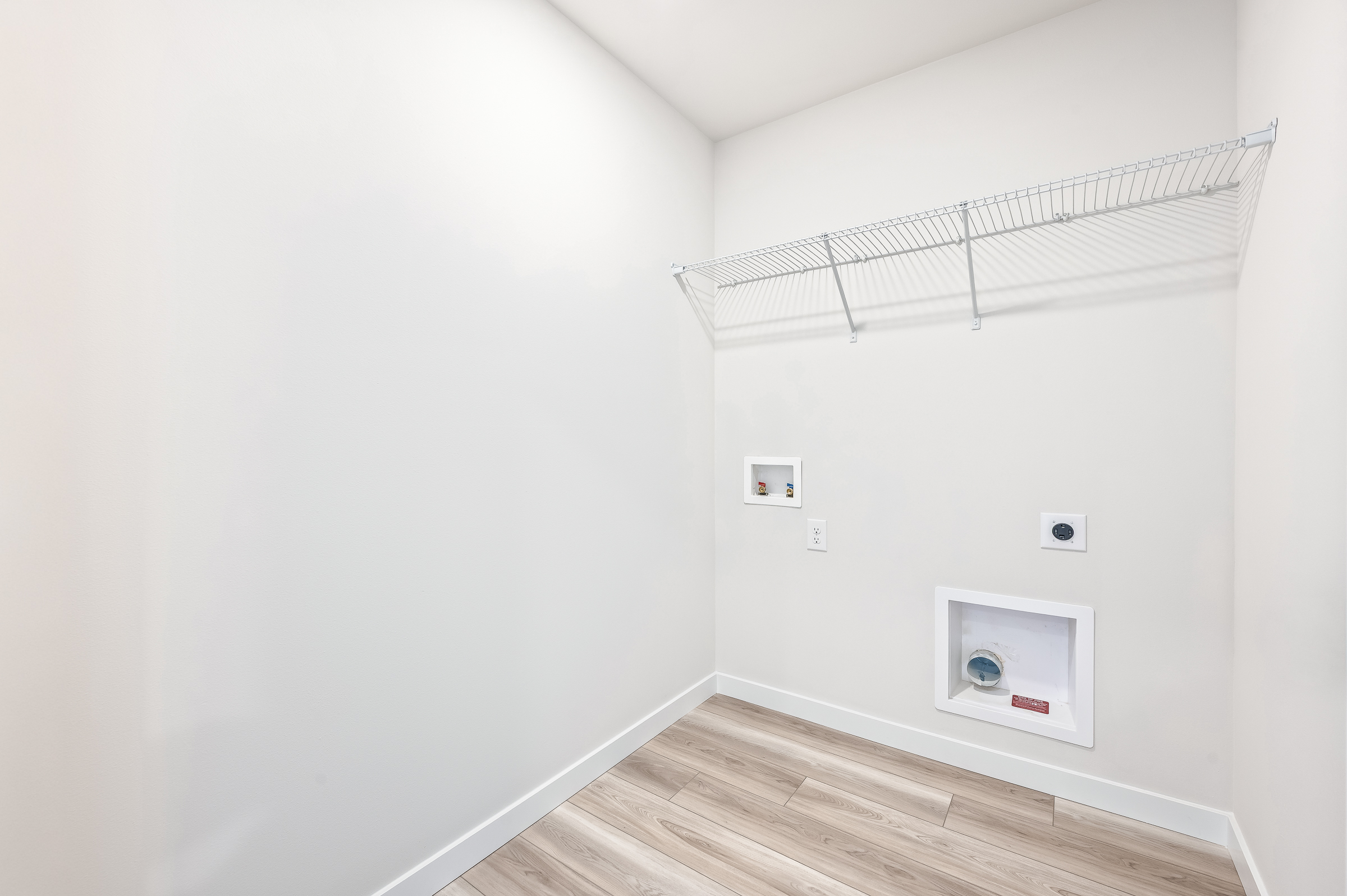 A room with a wood floor and a white wall with a vent.